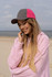 A woman with long hair smiles while wearing a pink and grey brushed heavy cotton cap at the beach.