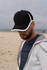A black cap with white trim, worn by a person on a beach, with a cloudy sky in the background.