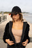A woman wearing a black cap with a hi-vis laminated two-tone peak, alongside a beach in the background.
