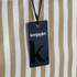 A striped beach tote bag in cream and tan, featuring a tag with a logo attached.