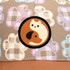 A cap featuring a light brown fabric with a playful paw print pattern and a circular patch displaying a cat and dog design.
