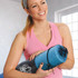 A yoga mat in a blue mesh bag, held by a smiling woman wearing a pink athletic top.