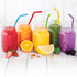 Five jars of brightly coloured drinks with silicone straws in red, blue, green, purple, and yellow, surrounded by fruit.