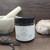 Northland Remedies Warm Vanilla Magnesium Lotion in a 4 oz amber glass jar, displayed next to an open jar of thick white topical cream, vanilla beans, lavender buds, and a white ceramic mortar and pestle on a dark wood background.