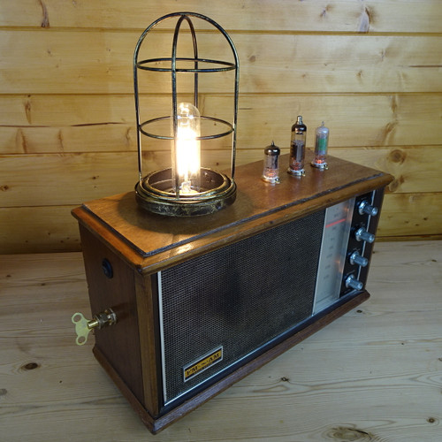 An individual hand-built steampunk lamp built from a vintage working 50-year old Sharp radio (transistor), with upcycled/vintage/new parts including a E27 weathered brass-effect cage, a radiator key and 3 illuminated thermionic radio valves (inactive) in new porcelain sockets