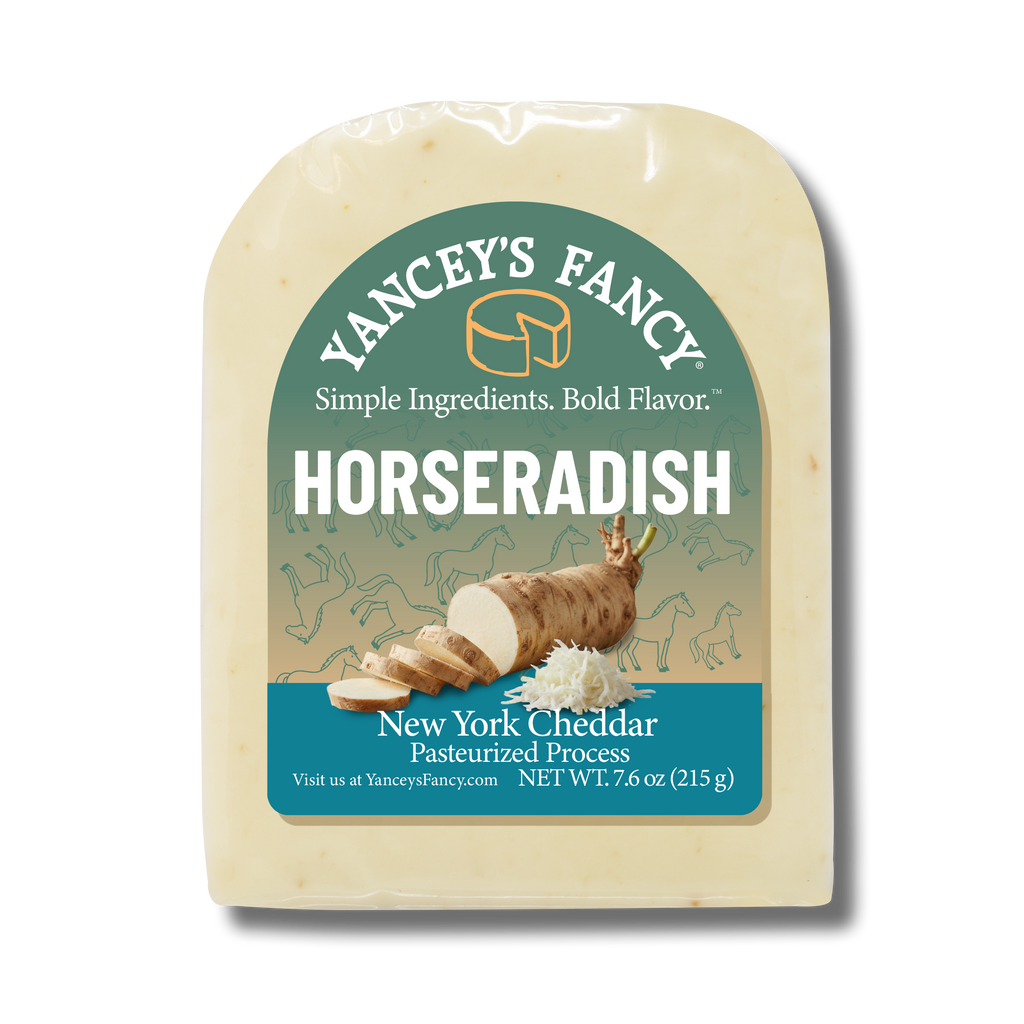 A vacuum-sealed block of Yancey's Fancy "Horseradish" New York Cheddar cheese. The arched label features a color palette that transitions from a muted teal-green at the top to a light tan in the middle, and finishes with a solid teal section at the bottom. The central illustration depicts a whole horseradish root, partially sliced into rounds, next to a small pile of freshly grated white horseradish. Faint line drawings of horses decorate the tan background section.

The text at the top reads "Yancey's Fancy" arched above the tagline "Simple Ingredients. Bold Flavor." The product name "HORSERADISH" is written in large, bold white capital letters. The teal bottom section reads "New York Cheddar Pasteurized Process" with a net weight of 7.6 oz (215 g). The block of cheese itself has a clean, uniform, creamy off-white color.