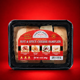 A plastic, vacuum-sealed sampler tray of Yancey's Fancy "Hot & Spicy Cheese Sampler" containing rows of pre-sliced cheese varieties. The arched label features a bright red wood-grain background. At the top of the arch sits the "Yancey's Fancy New York's Artisan Cheese" logo, with a small yellow "Pride of NY" emblem to its right. Below this, the product name "HOT & SPICY CHEESE SAMPLER" is written in a stylized white font.
The middle of the label displays four small square photos showing serving suggestions on crackers for each cheese variety included, listed from left to right:
Jalapeño & Piquante Cheddar: Paired with a red pepper slice.
Ghost Pepper Cheddar: Paired with a light jelly or jam.
Wasabi Horseradish Cheddar: Paired with a slice of roast beef.
Jalapeño & Cayenne Cheddar: Paired with a fold of deli meat.
The pre-sliced cheese slices are arranged neatly into four vertical rows matching the order on the label, showing off-white and pale green varieties peppered with spices. The bottom center indicates a net weight of 12 oz (340g), flanked by small dietary icons on the left and a barcode on the right.