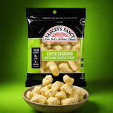 A bag of Yancey's Fancy Chive Cheddar Artisan Cheese Curds with cheese curds tumbling into a bowl. The packaging highlights 110 calories, 0g carbs, and 7g protein per serving against a vibrant green background.