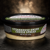 A tub of Yancey's Fancy Steakhouse Onion Cheese Spread, net weight 8 ounces (227 grams). The product features a black lid with a green and white logo, sitting on a dark rustic surface. The label on the front reads "STEAKHOUSE ONION CHEESE SPREAD" in bold white lettering against a faux woodgrain and green background. The container shows the creamy, light-colored cheese spread inside.