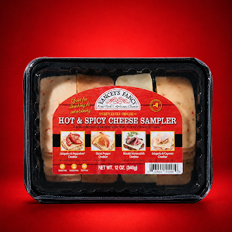 A plastic, vacuum-sealed sampler tray of Yancey's Fancy "Hot & Spicy Cheese Sampler" containing rows of pre-sliced cheese varieties. The arched label features a bright red wood-grain background. At the top of the arch sits the "Yancey's Fancy New York's Artisan Cheese" logo, with a small yellow "Pride of NY" emblem to its right. Below this, the product name "HOT & SPICY CHEESE SAMPLER" is written in a stylized white font.
The middle of the label displays four small square photos showing serving suggestions on crackers for each cheese variety included, listed from left to right:
Jalapeño & Piquante Cheddar: Paired with a red pepper slice.
Ghost Pepper Cheddar: Paired with a light jelly or jam.
Wasabi Horseradish Cheddar: Paired with a slice of roast beef.
Jalapeño & Cayenne Cheddar: Paired with a fold of deli meat.
The pre-sliced cheese slices are arranged neatly into four vertical rows matching the order on the label, showing off-white and pale green varieties peppered with spices. The bottom center indicates a net weight of 12 oz (340g), flanked by small dietary icons on the left and a barcode on the right.