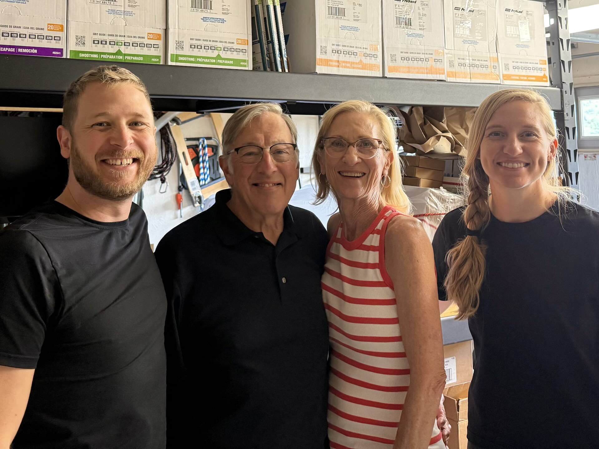 Photo of Tommy, Bruce, Julie, and Tori standing in front of the fulfillment area of US Paint Supply