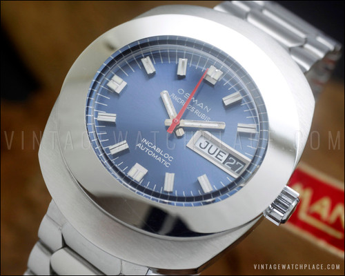 NOS Osman automatic vintage watch with blue dial, raised silver-tone indexes, red central seconds hand, framed Spanish day-date window and original stainless steel bracelet.