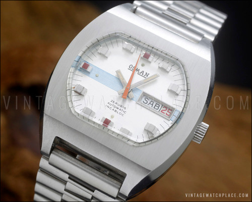 NOS Osman automatic vintage watch in stainless steel, with silver dial, light blue striped accent, red marker details, orange central seconds hand, Spanish day-date calendar and original steel bracelet.