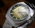 Opposite three-quarter view of the Sakay 61365A NOS automatic watch, highlighting the faceted case, raised crystal, integrated steel bracelet and green textured dial.