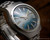 Angled close-up of the Osman 2378W3 automatic watch, highlighting the blue sunburst dial, applied markers, hands and day-date window.