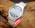 Angled view of the New Old Stock Osman 2378W3 automatic, showing the green textured dial, stainless steel case, original bracelet and red hang tag.