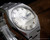 Angled close-up of the Osman 982 silver dial, highlighting the raised indexes, hands, minute track and framed day-date window.