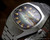 Close-up view of the Osman NS6633 automatic dial, showing the purple-green gradient striped finish, raised hour indexes, Spanish day-date calendar and faceted crystal.