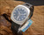 New Old Stock Titan Submerger automatic watch displayed on wood, showing the blue-grey dial, stainless steel cushion case, original Titan hang tag and NOS RK Swiss Made strap.