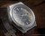 Angled close-up of the Tecnal smoky brown-grey dial, showing the applied indexes, pale green luminous paste, day-date window and visible age signs.