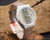Angled view of the Tecnal automatic vintage watch on wood, highlighting the smoky dial, framed day-date calendar, original crown and vintage-style strap.