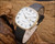 New Old Stock Leo Andreotti automatic watch displayed on wood, with white dial, Roman numerals, gold-tone case and black leather strap.
