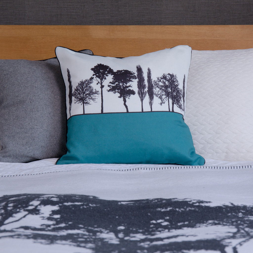 Teal English countryside landscape cushion shown on bed, by designer Jacky Al-Samarraie