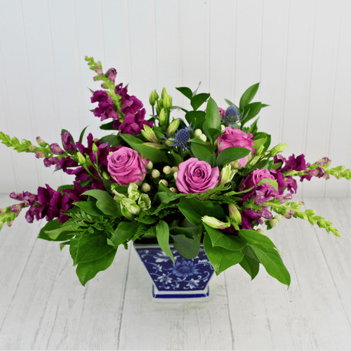 Violet Avenue flower arrangement featuring lavender roses and purple snapdragons in a blue patterned ceramic vase.