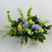 Summer Social flower arrangement featuring blue hydrangeas, yellow roses, and tall green bells of Ireland in a white pedestal container.
