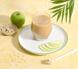 Herbalife Oat Apple Fibre Drink (204g). Glass of a Herbalife Oat Apple Fibre on a plate with sliced apples, an apple, and a bowl of oats.