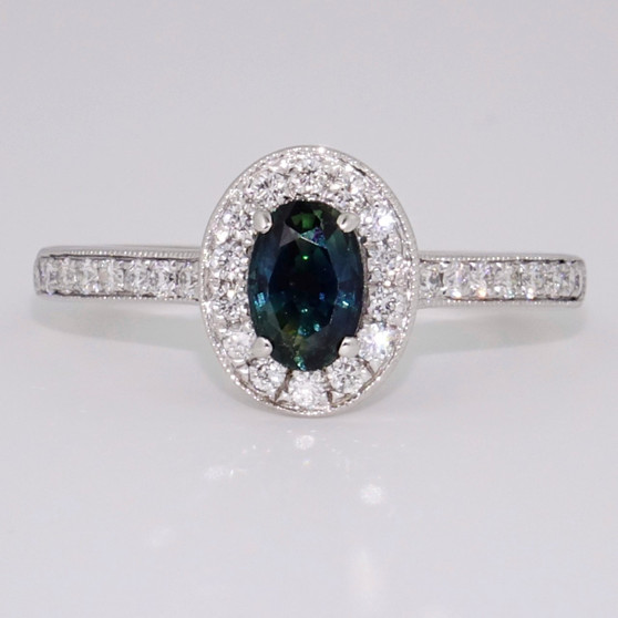9ct white gold oval cut teal sapphire and round brilliant cut diamond cluster ring with diamond-set shoulders and a milgrain edge