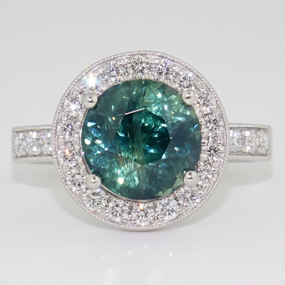 Platinum round cut teal sapphire and diamond halo ring with diamond-set shoulders and milgrain edge