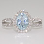 Platinum oval cut aquamarine and round brilliant cut diamond halo ring with open diamond-set shoulders