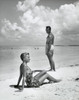 Side profile of young woman sitting with young man standing on beach Poster Print - Item # VARSAL255338