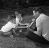 Father with twin sons reading book sitting on lawn Poster Print - Item # VARSAL255418297