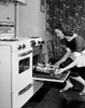 Young woman taking baked food out of oven Poster Print - Item # VARSAL255416690
