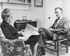 Senior woman reading a newspaper with a senior man sitting in front of her Poster Print - Item # VARSAL2558598