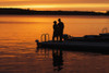 Silhouette of a couple standing at the end of a dock at sunset with an orange glow in the sky and reflected in the tranquil lake water; Ontario, Canada PosterPrint - Item # VARDPI12303007