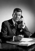 Mid adult man sitting at desk talking on phone Poster Print - Item # VARSAL255417019
