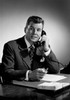 Mid adult man sitting at desk talking on phone Poster Print - Item # VARSAL255417019