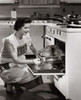 Side profile of a mid adult woman putting a turkey into an oven Poster Print - Item # VARSAL25519584