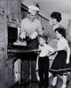 Mid adult man taking food out of an oven with his family standing beside him Poster Print - Item # VARSAL25536213