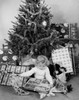 Girl sitting in front of a Christmas tree and opening a Christmas present Poster Print - Item # VARSAL25516081