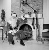 Portrait of Santa Claus sitting in front of a fireplace and holding a Christmas present Poster Print - Item # VARSAL255700