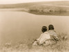 Two Piegan Indians sitting on grassy area above a body of water. Poster Print - Item # VARBLL058746951L