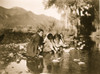 Four Taos children squat on rocks at edge of stream, mountains in background. Poster Print - Item # VARBLL058747596L