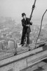 Cameraman in suit holds onto cable as he walks unharnessed over a skyscraper's steel girders Poster Print by unknown - Item # VARBLL0587243392