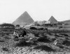 Two people sitting on rocks in an area of sparse vegetation in front of the Mena House Hotel, two pyramids in background Poster Print by Felix Bonfils - Item # VARBLL0587419830