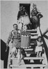 Two Indians descending wooden stairs carrying drums; another Indian and child near by "Dance San Ildefonso Pueblo New Mexico 1942." 1942 Poster Print by Ansel Adams - Item # VARBLL0587401095