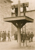 Ground level whipping post, above which is a platform for the pillory, presently occupied by two African American men; a ladder leans against the platform, a group of men loiter in the background. Poster Print - Item # VARBLL0587634596